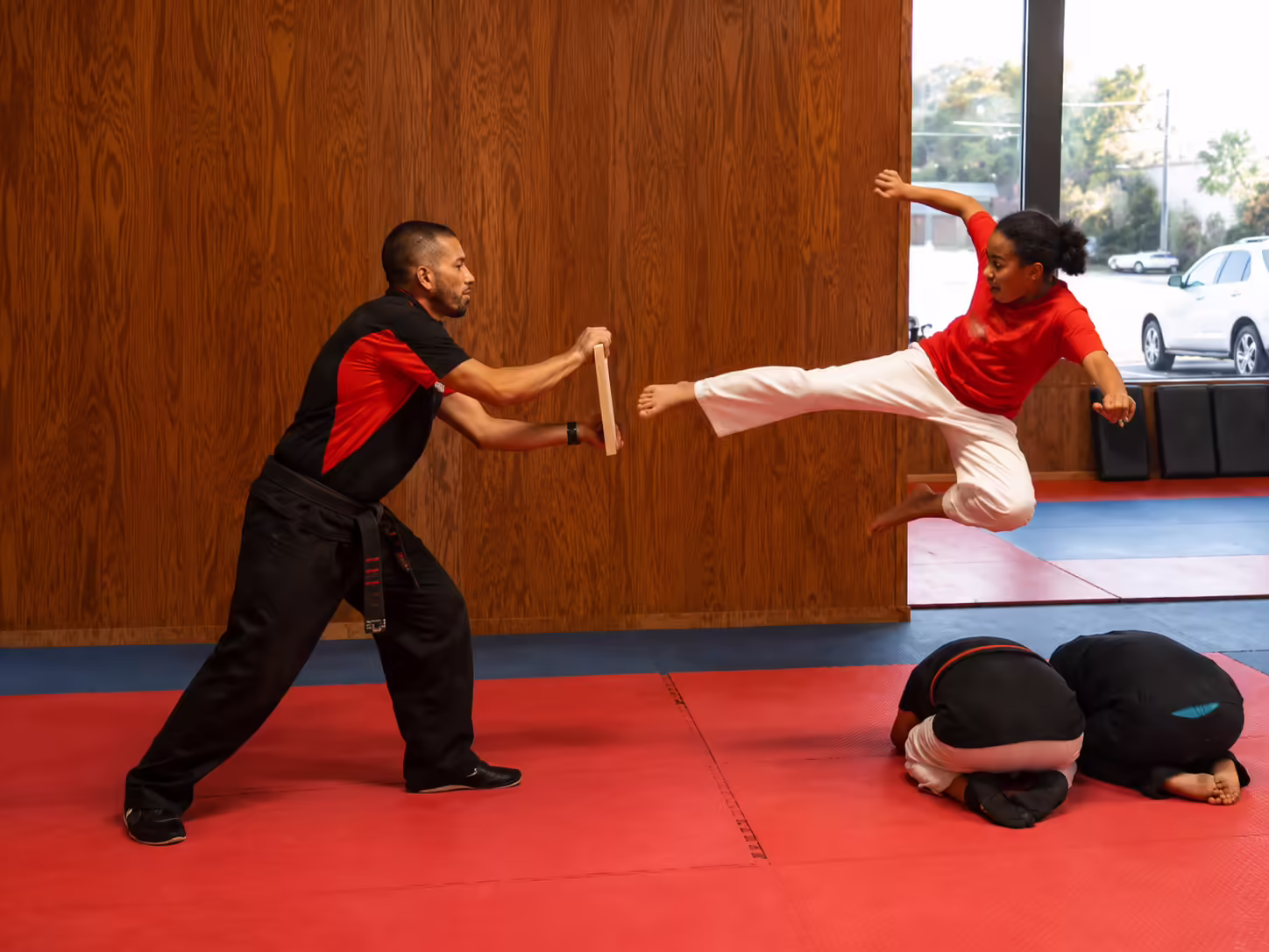 Taekwondo student jumping over classmates and breaking a board with a kick at Dunedin Taekwondo Academy